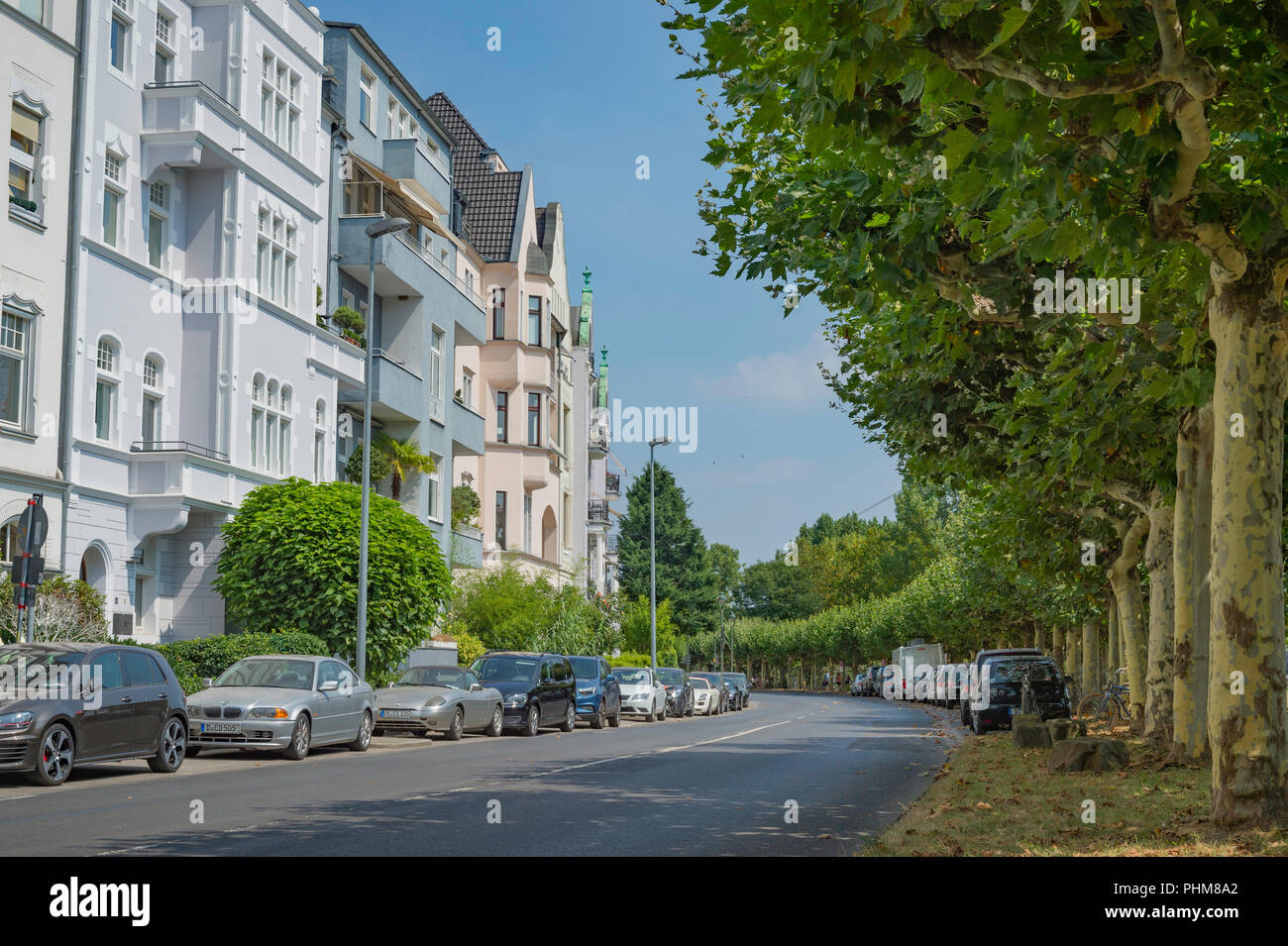 Autos auf einer kurvigen Straße mit Bäumen ein Apartment Gebäude in Düsseldorf, Deutschland gesäumt geparkt. Stockfoto