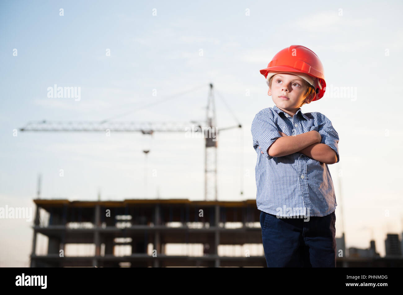 Stattlichen amerikanischen kaukasischen Kind in orange Helm auf der Baustelle mit Kran Stockfoto