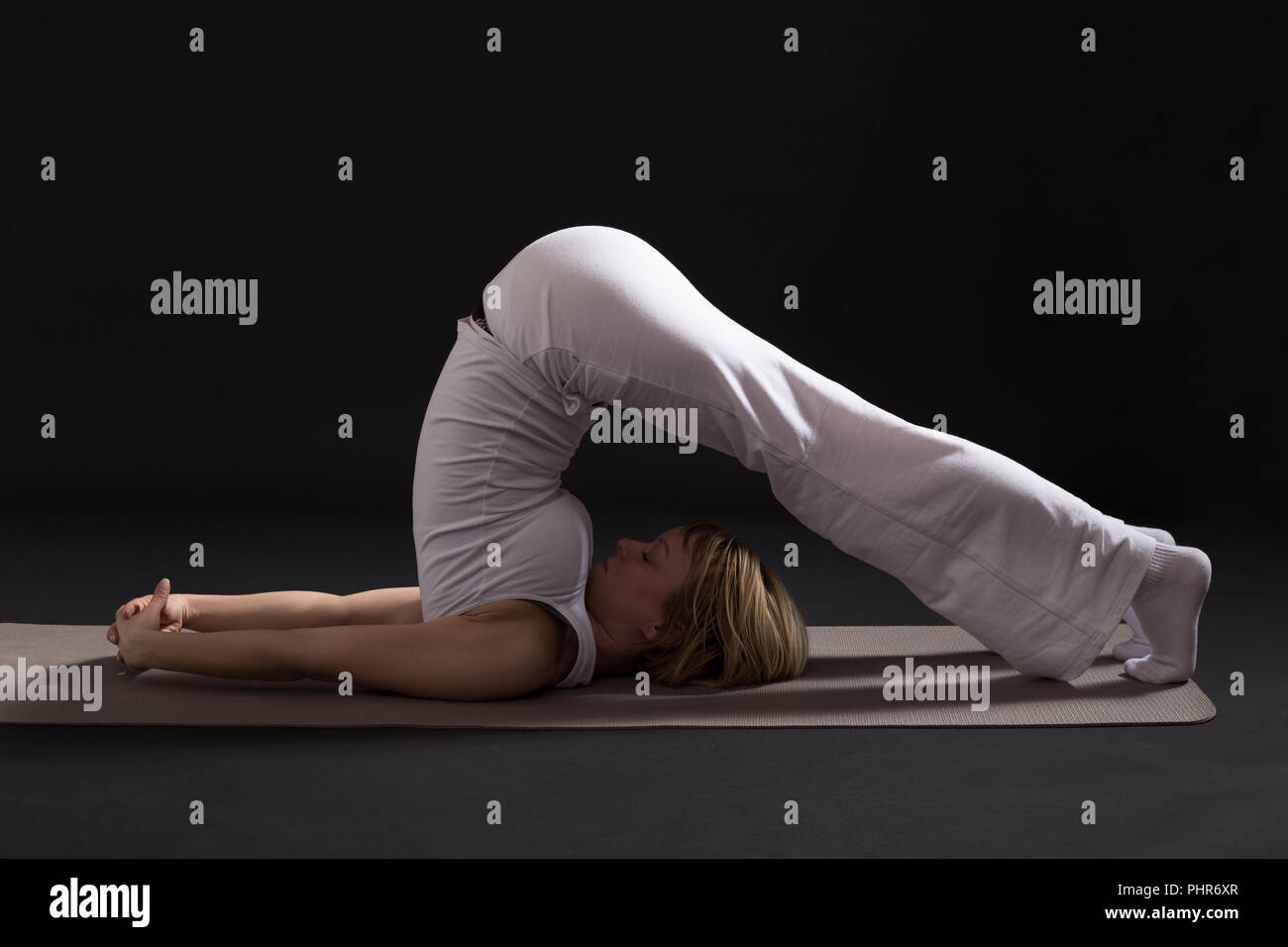 Frau trainieren Yoga indoor auf schwarzem Hintergrund, Pflug pose/Halasana Stockfoto