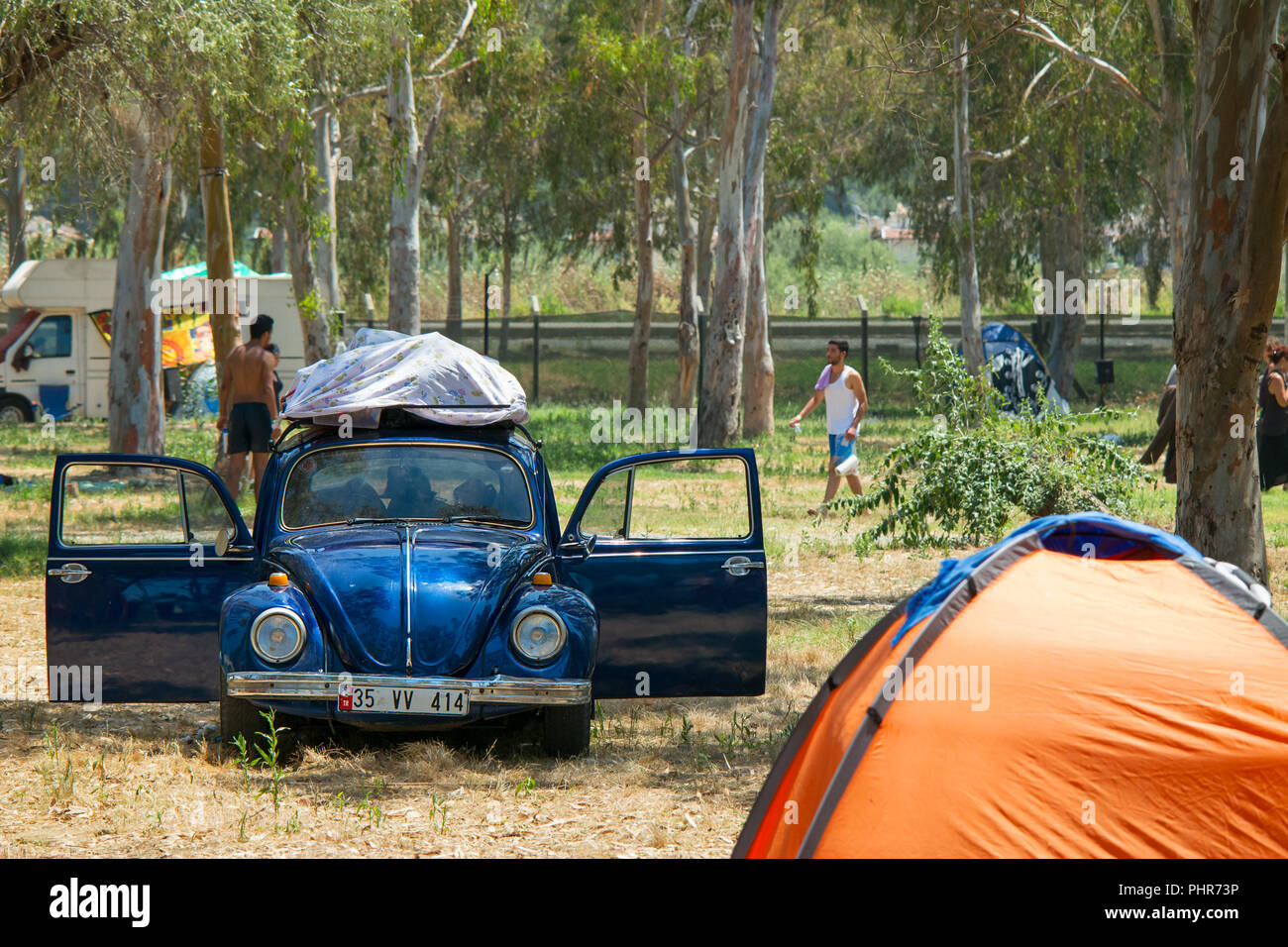 Ein classic Blau VW Käfer bis in den Schatten mit den Türen an einem heißen sonnigen Tag auf einem Campingplatz mit Camper im Hintergrund offen geparkt. Stockfoto