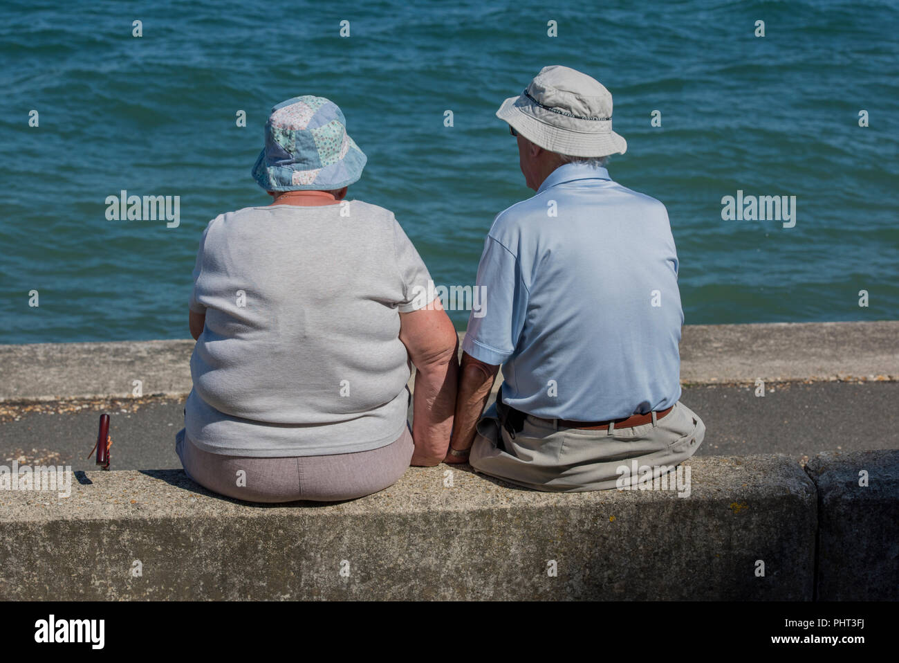 Ein älteres Paar trägt eine Mütze auf dem Kopf sitzen Hand in Hand am Meer mit Meerblick. Stockfoto