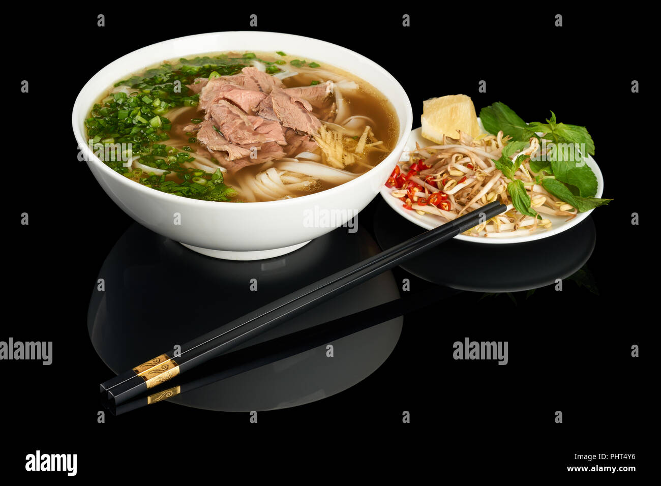 Platte der vietnamesische Nudelsuppe Pho Bo isoliert auf schwarzen Hintergrund reflektieren. Mit Stäbchen, Sojasprossen und Chili serviert. Stockfoto