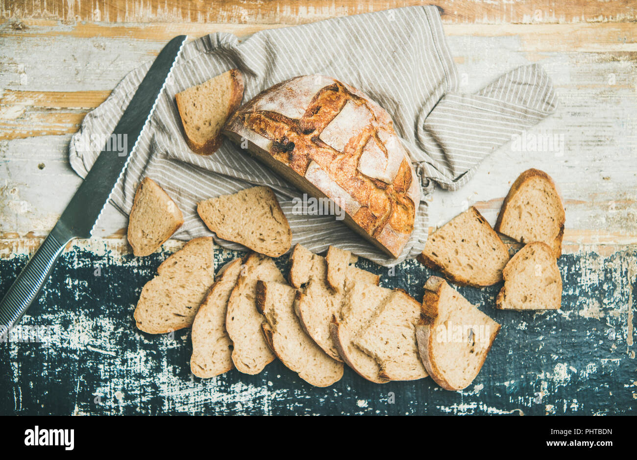 Flachbild-lay von frisch gebackenem Sauerteig Brot aus Weizen Brot halbieren und in Scheiben über Bettwäsche Serviette und rustikalen Tisch Hintergrund ausschneiden, Ansicht von oben, horizontal Comp Stockfoto