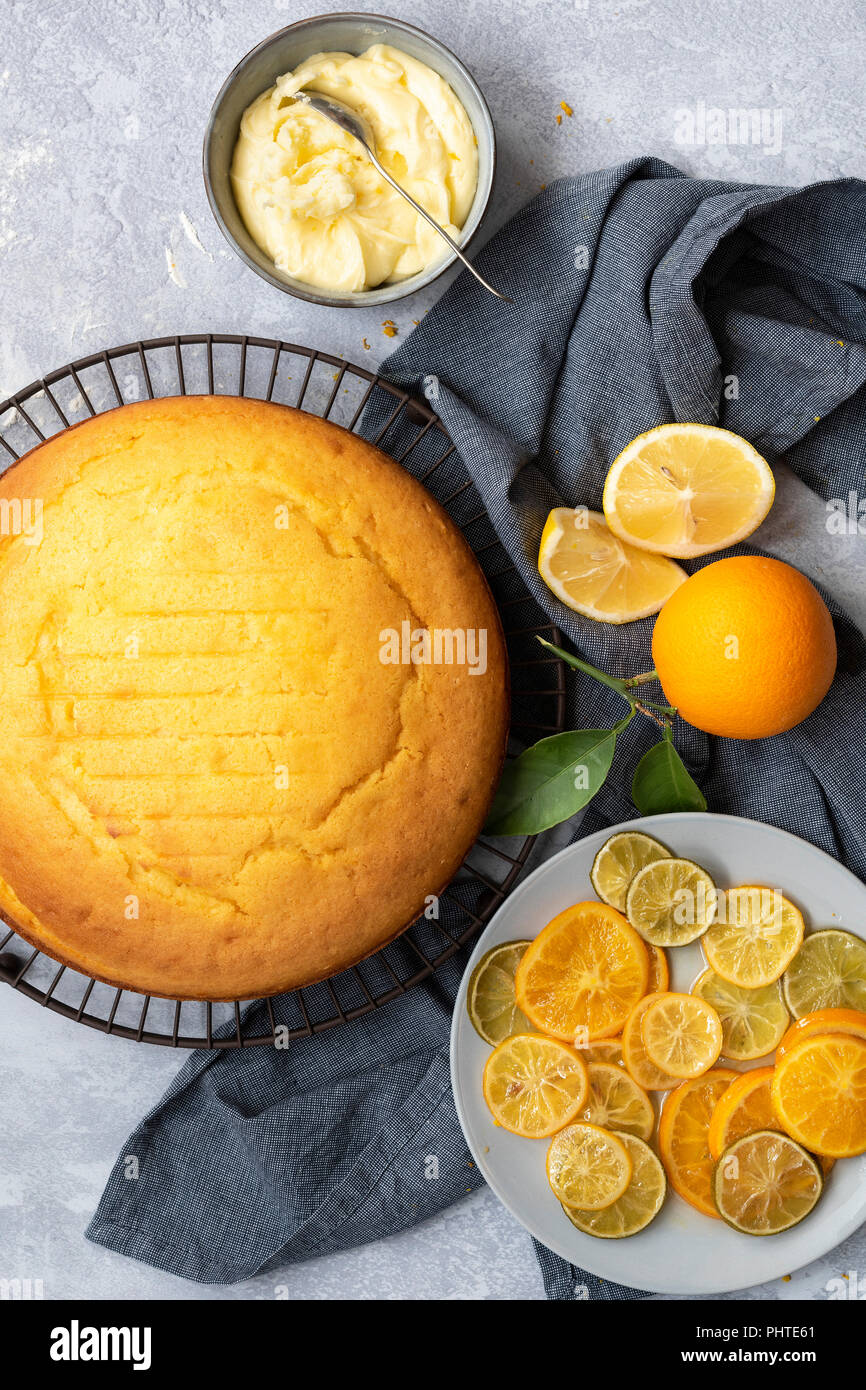 Eine Runde hausgemachte orange Kuchen mit einer Platte von geschnittenen kandierten Zitrusfrüchten und einer Schüssel Butter Puderzucker. Stockfoto