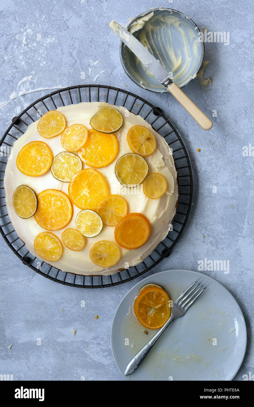 Eine Runde hausgemachte orange Kuchen mit Butter und Puderzucker mit kandierten Zitronen, Limetten und orangen Scheiben eingerichtet. Stockfoto