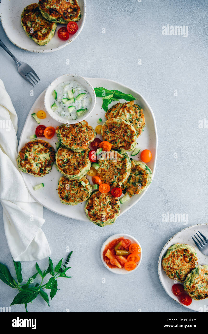 Zucchini Krapfen auf einer Keramikplatte mit Trauben Tomaten und Joghurt dip auf der Seite von der Ansicht von oben fotografiert. Zwei kleinere Platten und Frische mi Stockfoto