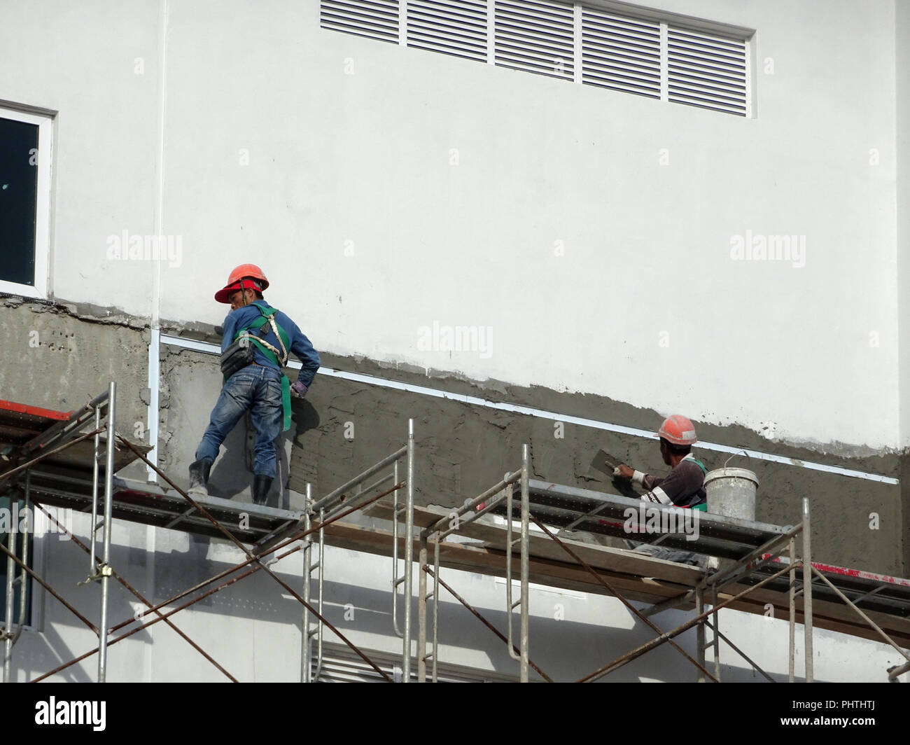 Bauarbeiter verputzarbeiten Wand mit Zementputz auf der Baustelle. Sie sind das Tragen geeigneter Schutzausrüstung schlecht geschehen zu verhindern. Stockfoto