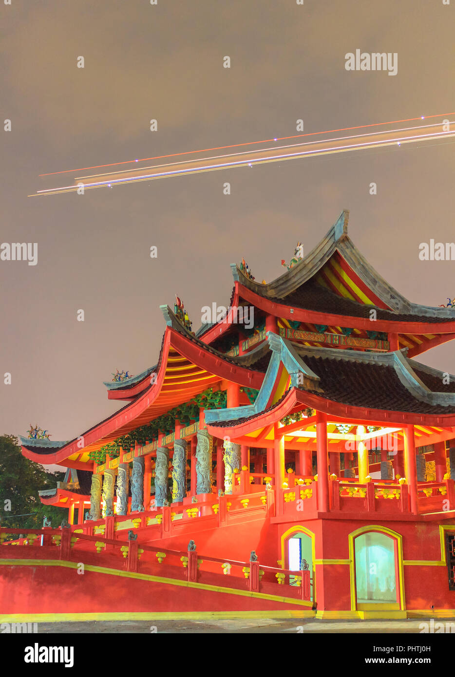 Eine Langzeitaufnahme des Sam Poo Kong Tempels bei Nacht, mit einem Flugzeug, das über dem Himmel vorbeifährt und seine leuchtende Architektur und sein reiches Erbe unterstreicht Stockfoto