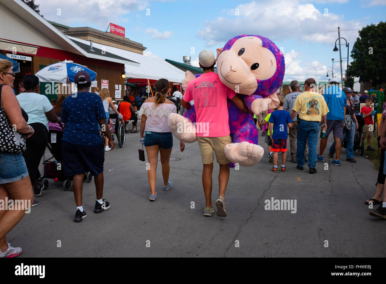 Der Mensch trägt große Stofftier gewann er das Spielen ein Karneval Spiel am Great New York State Fair, 1. September 2018. Stockfoto