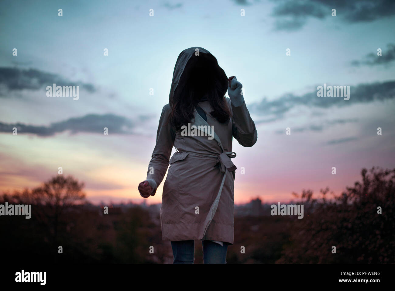 Die anonyme Frau bekleidet mit Kapuze Trenchcoat Tanz in den Sonnenuntergang. Geheimnisvoll, kreativ-travel/lifestyle Konzept. London, Großbritannien Stockfoto