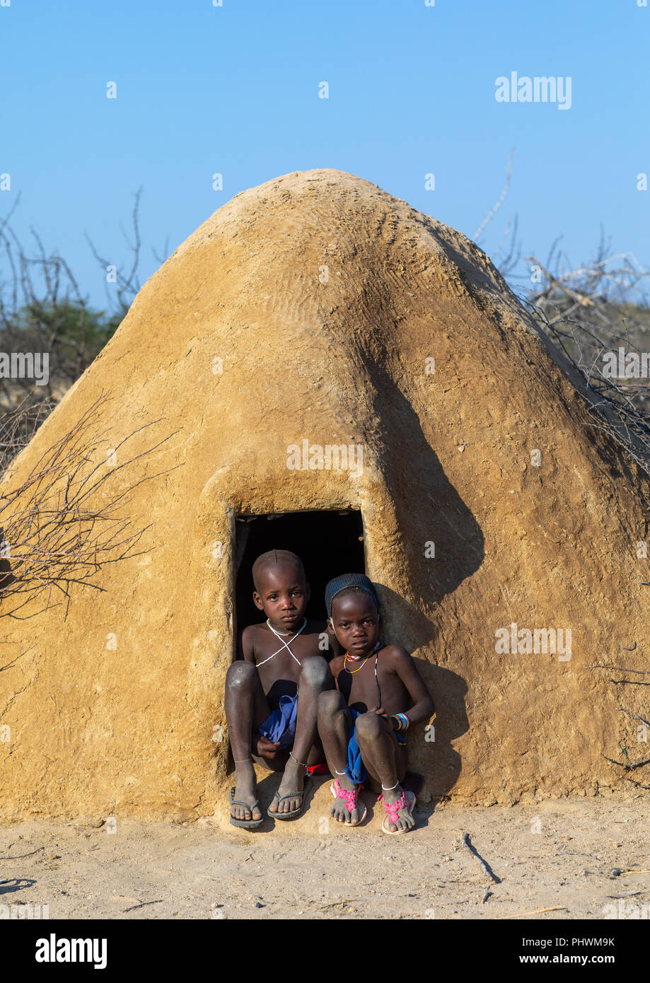 Mucubal Stamm Kinder am Eingang Ihrer Hütte bedeckt von Adobe sitzen, Provinz Namibe, Virei, Angola Stockfoto