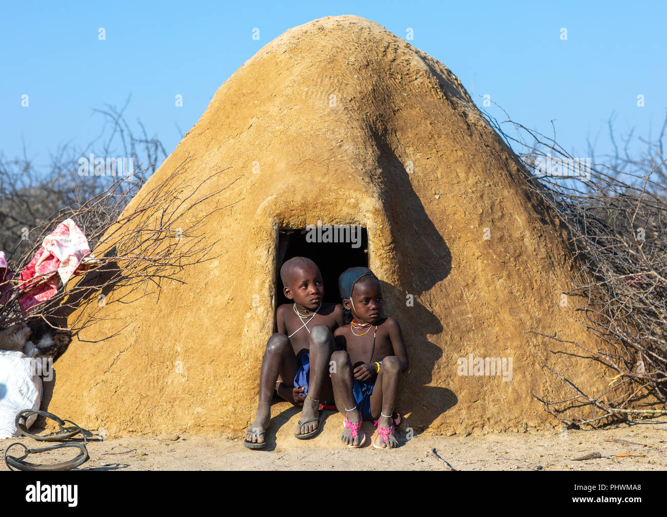 Mucubal Stamm Kinder am Eingang Ihrer Hütte bedeckt von Adobe sitzen, Provinz Namibe, Virei, Angola Stockfoto