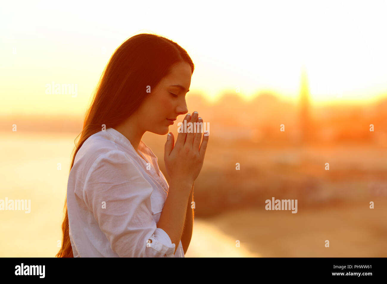 Profil von einer konzentrierten Frau mit Händen gemeinsam beten bei Sonnenuntergang Stockfoto