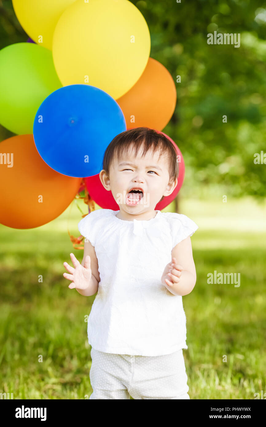 Portrait von cute adorable asiatischen Mädchen Kind ein Jahr alt in weißem Hemd mit Ballons auf dem Feld Wiese Park außerhalb, gepäckdurchleuchtung in Angst Stress, Konzept o Stockfoto