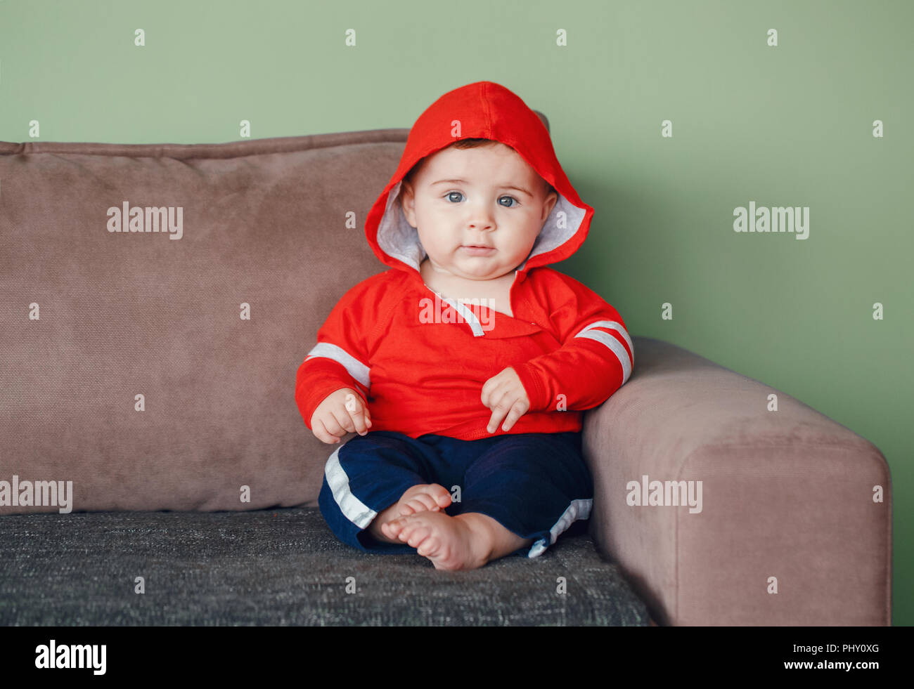 Portrait von cute adorable Kaukasischen smiling baby Junge mit blauen Augen, das Tragen der roten Sport Jogginganzug hoodie Shirt und Hose. Sieben Monate Kind auf Sitzung Stockfoto