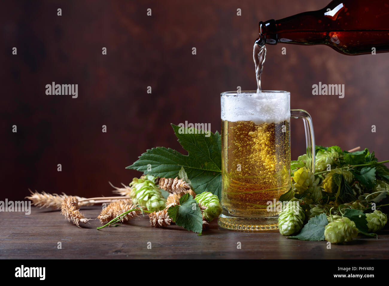 Becher Bier, Korn und Hopfen auf einem alten Holztisch. Bier ist in einem Becher aus der Flasche gegossen. Freier Platz für Text. Stockfoto