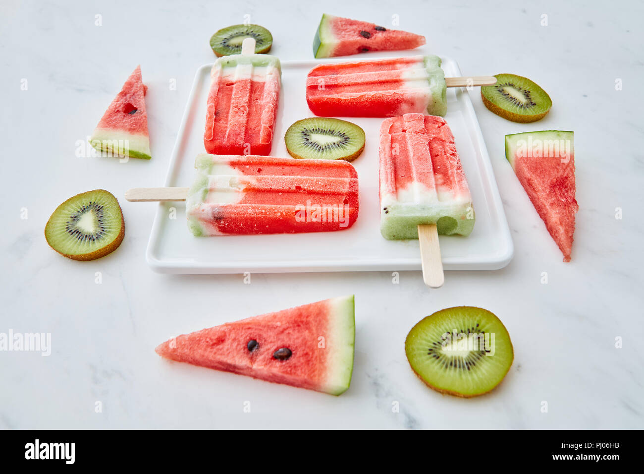 Scheiben Wassermelone und Kiwi in der Form eines Kreises und ein Dreieck um eine Platte mit einem gesunden Eis lolly in Form eines Vierecks auf grauem Marmor Hintergrund. Essen Muster. Stockfoto