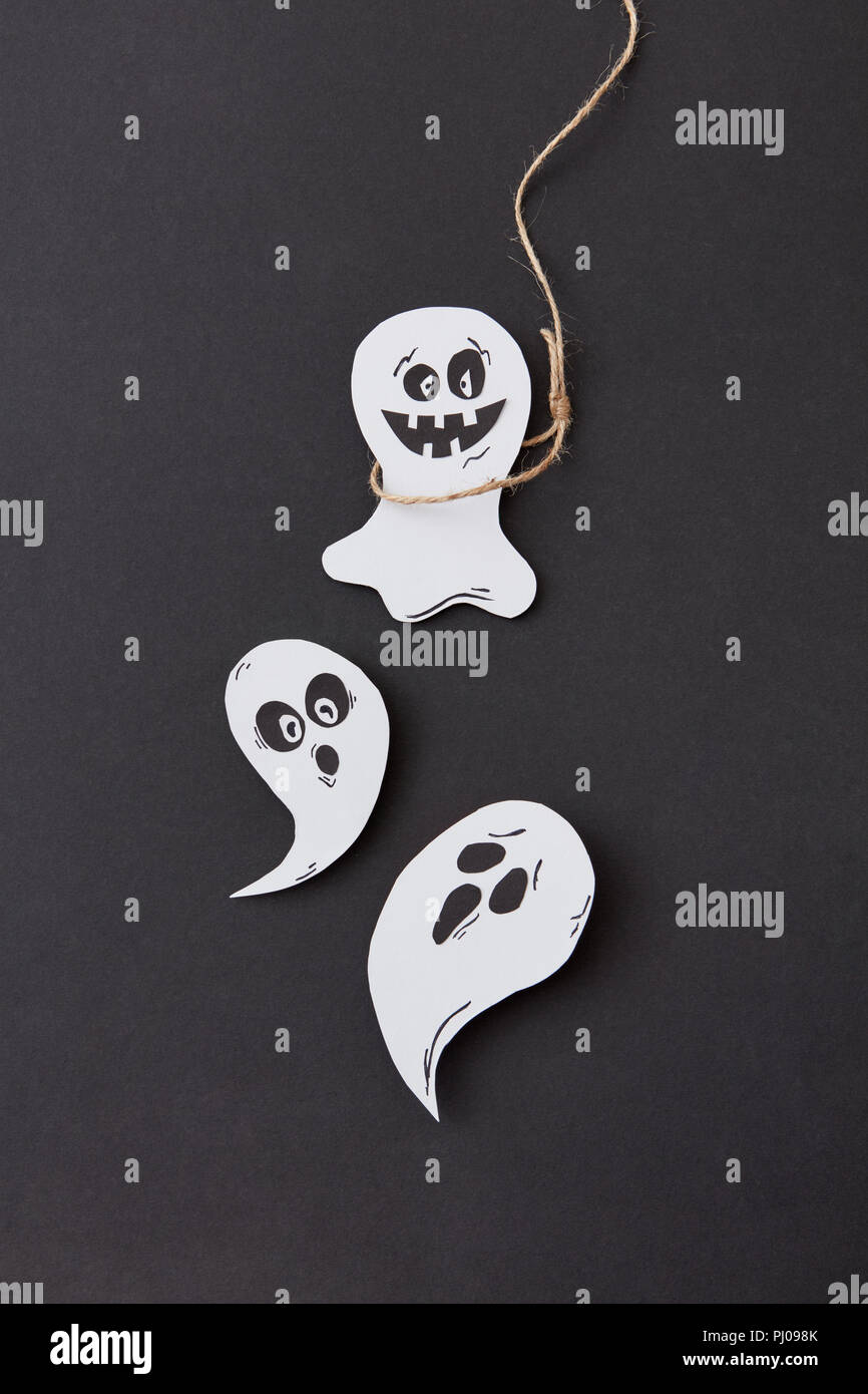 Kreative Halloween Card mit Lachen flying scary Gespenst und Ghost am Seil handgefertigt aus Papier auf einem schwarzen. Stockfoto