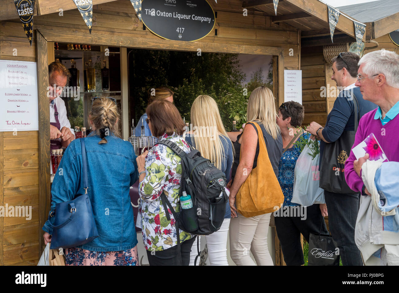 Menschen diente, Kauf & Queuing für handgefertigte Liköre in Glasflaschen am Messestand Hütte - RHS Chatsworth Flower Show, Derbyshire, England, UK. Stockfoto