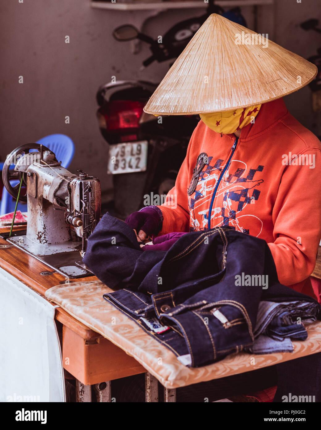 Nha Trang, Vietnam - Mai 5, 2018: ein Schneider in einem Reis hat und eine Maske (das ihr Gesicht verstecken) arbeitet mit Jeans am Tisch mit einer alten Nähmaschine. Stockfoto