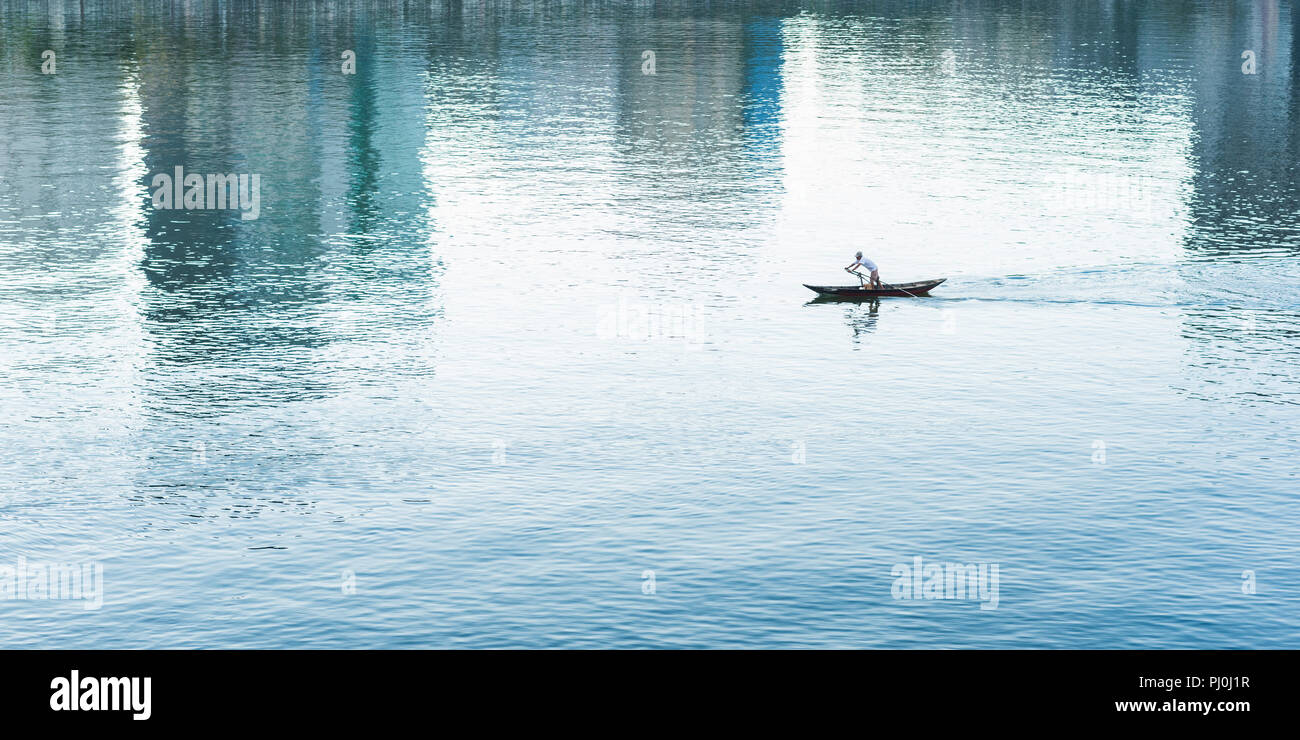 Boatman Zeilen durch das Wasser Welligkeit, mehrstöckigen Gebäuden und den Himmel. Dies ist Stadt Da Nang, Vietnam in der Reflexion auf den Fluss Han Stockfoto