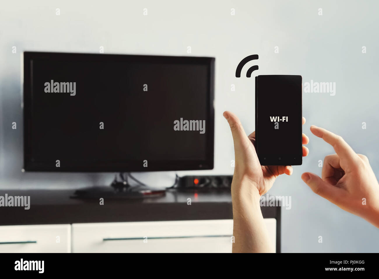 Männliche hand mit einem Smartphone. Steuern Sie Ihren Fernseher mit Smartphone. Konnektivität zwischen Smart TV und Smart Phone durch Wifi Verbindung zu verteilen. Stockfoto