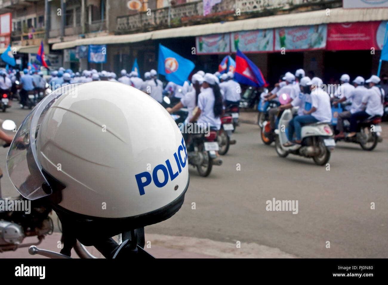 Kambodschanische Volkspartei (CPP) Anhänger Motorräder fahren an einem Polizisten Helm während einer Wahlkampfveranstaltung in Kampong Cham, Kambodscha. Stockfoto