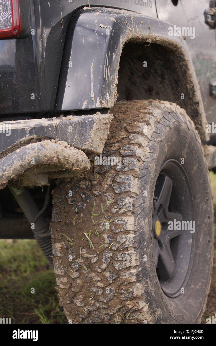 In der Nähe von verschmutzten SUV nach aus schweren Fahren - Straße in nassem Terrain. Räder verschmutzt in Schlamm und Schmutz. Stehend auf grünem Gras Oberfläche. Stockfoto