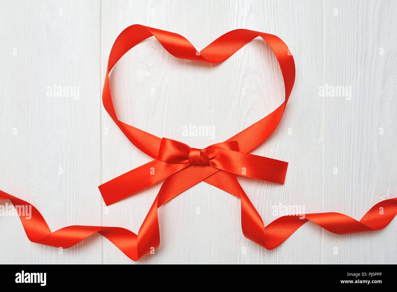 Herz aus roten Schleife auf weißem Holz- Hintergrund. Romantische Liebe Konzept. Valentines Tag Hintergrund für Geburtstag, Urlaub, Party, Hochzeit. Flach. Stockfoto
