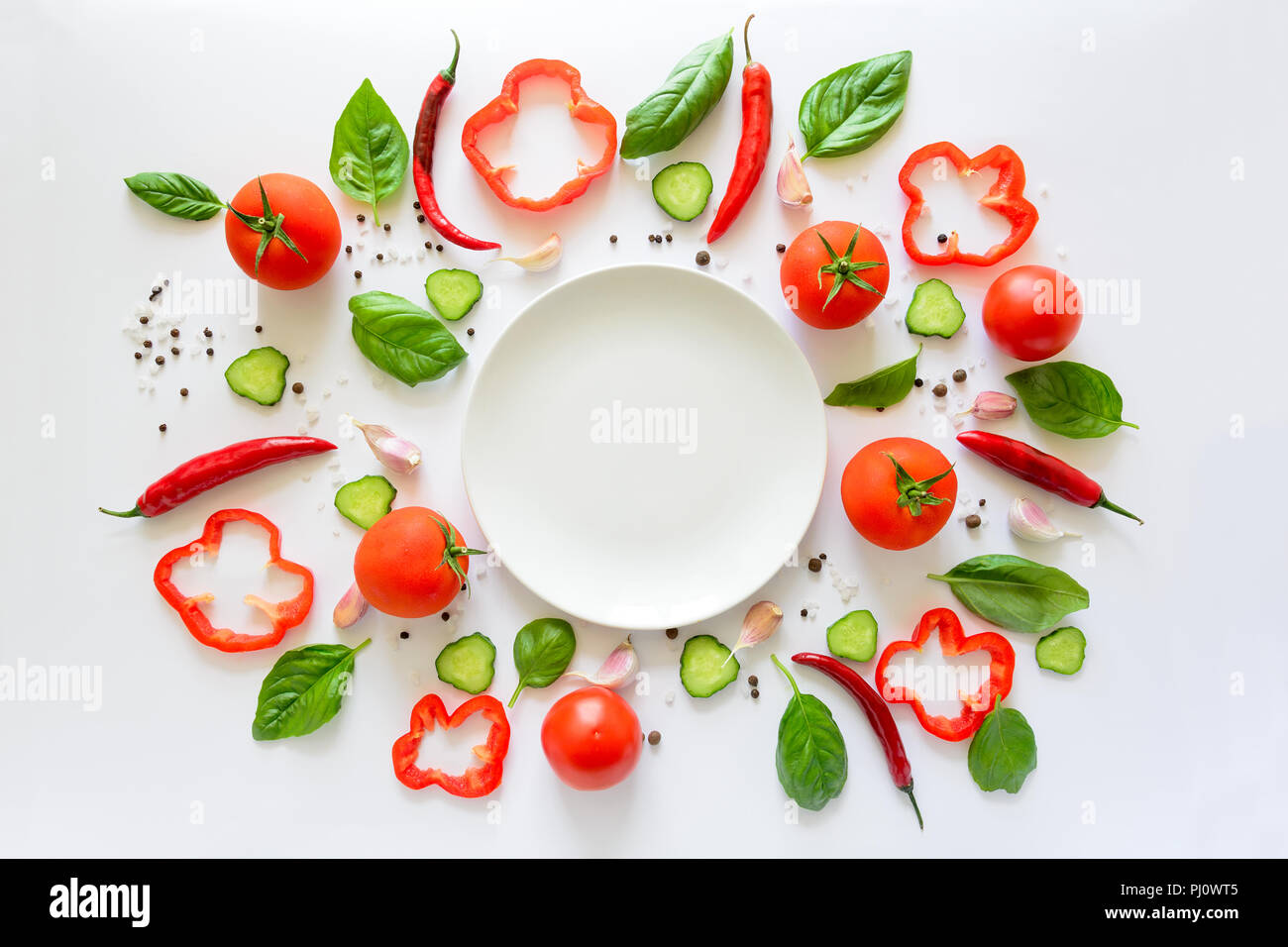 Bunter Salat Zutaten Muster aus Tomaten, Pfeffer, Chili, Knoblauch, Gurkenscheiben, Basilikum und leeren Teller auf weißem Hintergrund. Kochen conce Stockfoto