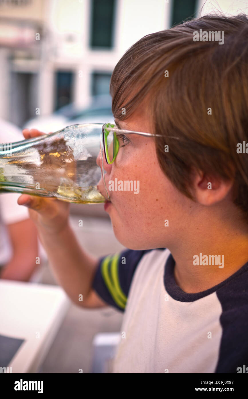 Nahaufnahme der Seite Profil der elf Jahre alten Jungen mit Brille aus einem Glas trinkt, das auf einer Terrasse in einem Café in Spanien Stockfoto