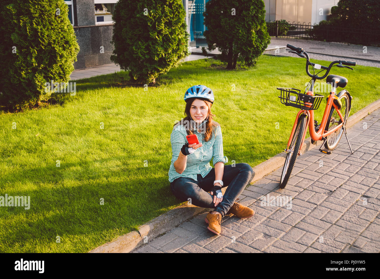 Mensch und Stadt rollenden Fahrrad, umweltfreundliche Verkehrsmittel. Schönen jungen kaukasischen Arbeiterin sitzen ruht auf dem Gras verwendet eine rote mobil Stockfoto