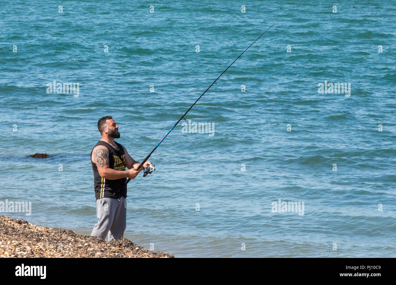 Ein Mann stand am Strand in der Nähe des Meeres mit einer Angelrute. Meeresangeln oder Angler. Stockfoto