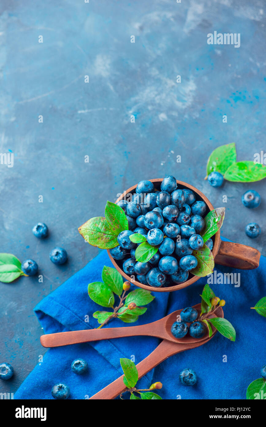 Sommer Beeren flach. Heidelbeeren im keramiktasse mit holzlöffel von oben. Neutrale Farben, Blau und Grau Palette, kopieren Raum Stockfoto
