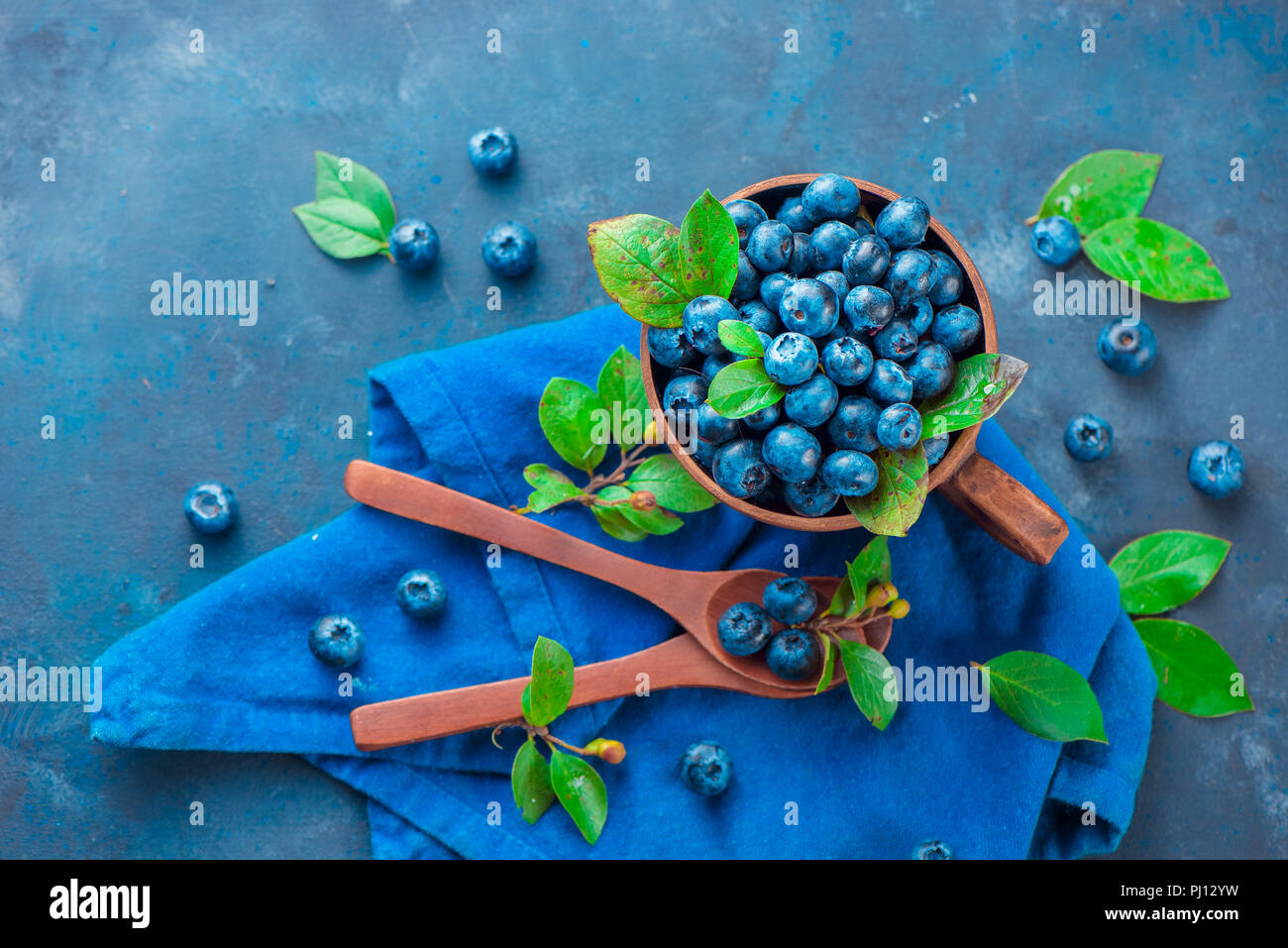 Heidelbeeren im keramiktasse mit holzlöffel und ein Bettwäsche Serviette. Reif und süß Sommer Beeren auf einem Stein. Neutrale Farben, Blau und Grau Stockfoto