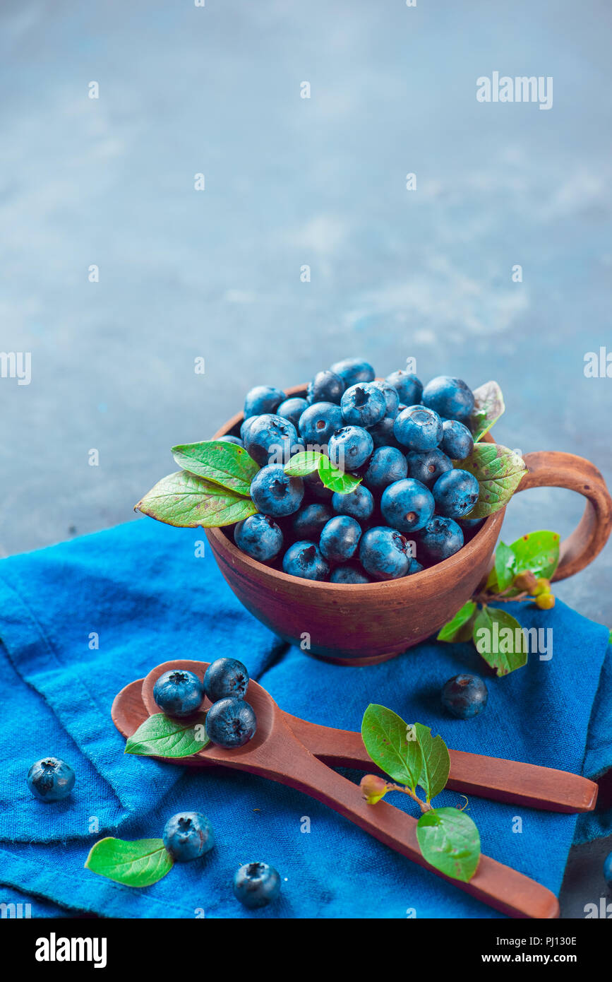 Heidelbeeren im keramiktasse mit holzlöffel und ein Bettwäsche Serviette. Reif und süß Sommer Beeren auf einem Stein. Neutrale Farben, Blau und Grau Stockfoto