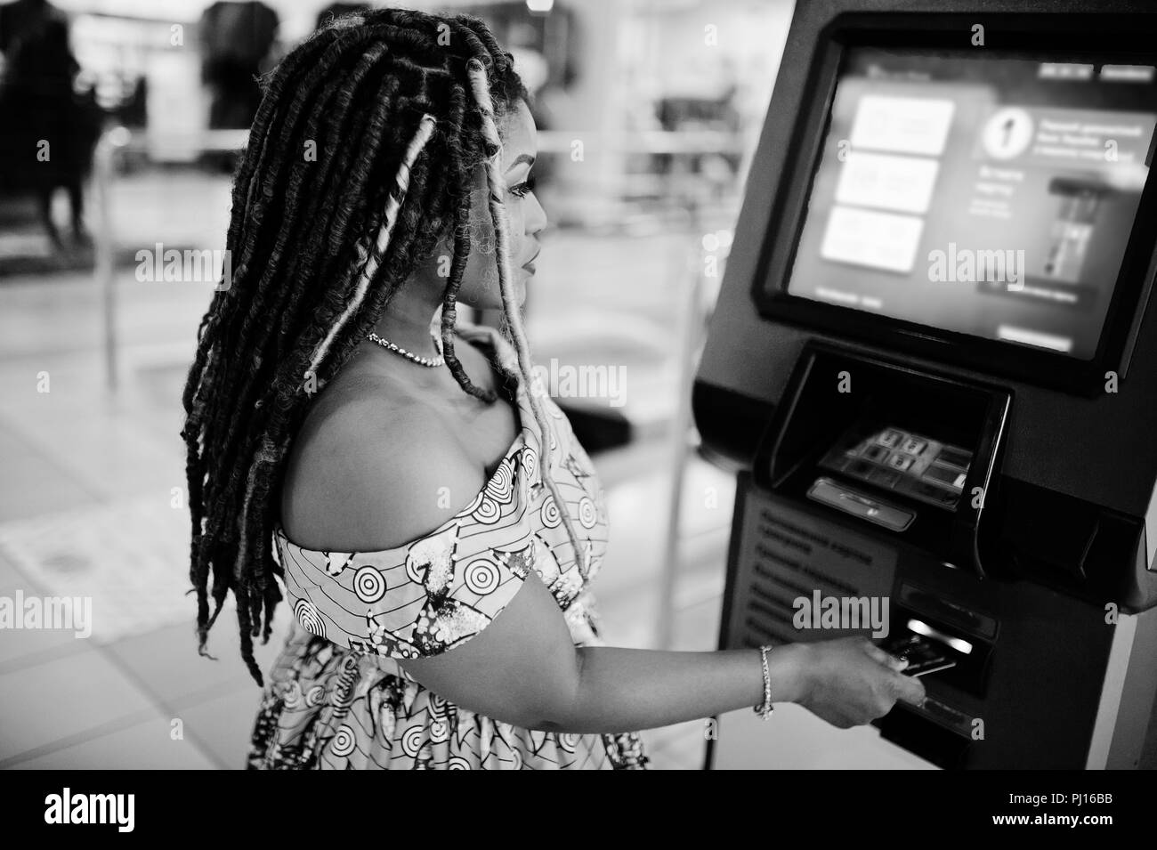 Süße kleine Höhe afrikanische amerikanische Mädchen mit Dreadlocks, Verschleiß an den Farben gelb kleid, gegen ATM mit Kreditkarte zur Hand. Schwarz und Weiß. Stockfoto