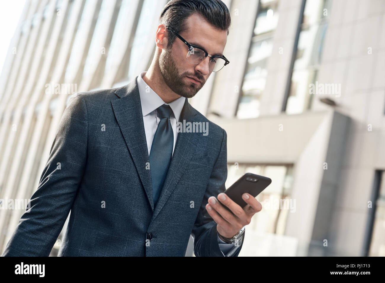 Gut aussehender junger Mann, der in einen kompletten Anzug mit seinem Smart Phone beim Stehen im Freien Stockfoto