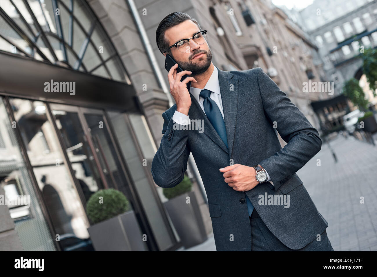 Auf dem Weg zu Geschäftstreffen. Gut aussehender junger Mann in Smart Casual Wear über sein Smartphone und lächelnd während zu Fuß durch die Stadt. Stockfoto