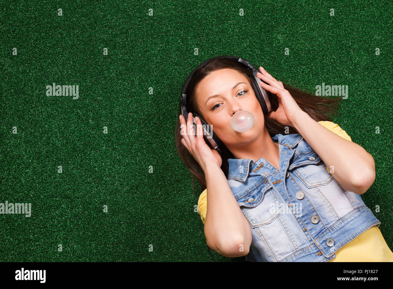 Fröhliche junge Frau mit Kopfhörer genießt in der Musik und blasen Blase im Liegen auf Gras Stockfoto