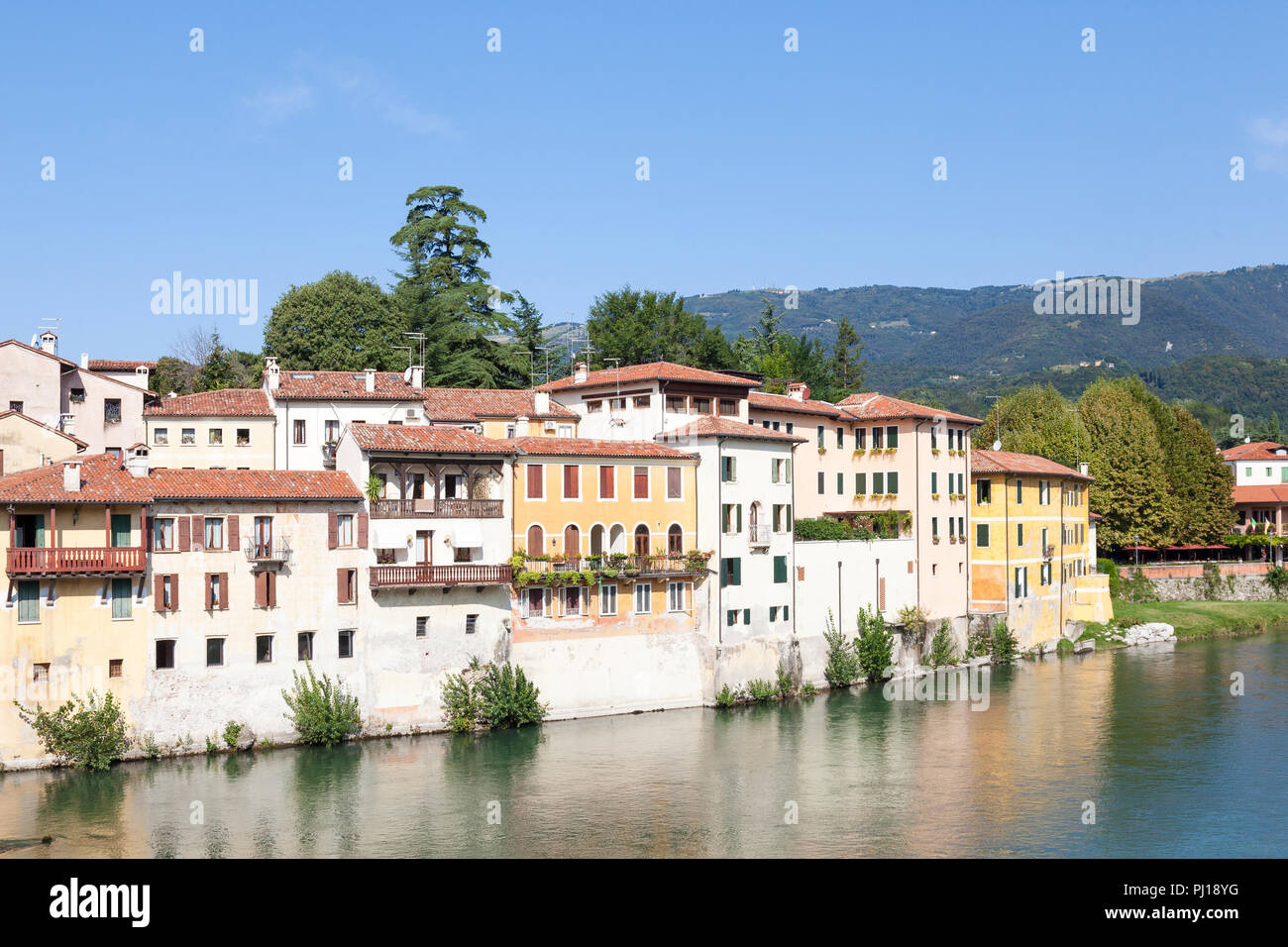 Bunte Häuser auf dem Brenta Fluss, Bassano del Grappa, Vicenza, Italien im frühen Morgenlicht mit Reflexionen und Blick auf die Dolomiten. Stockfoto