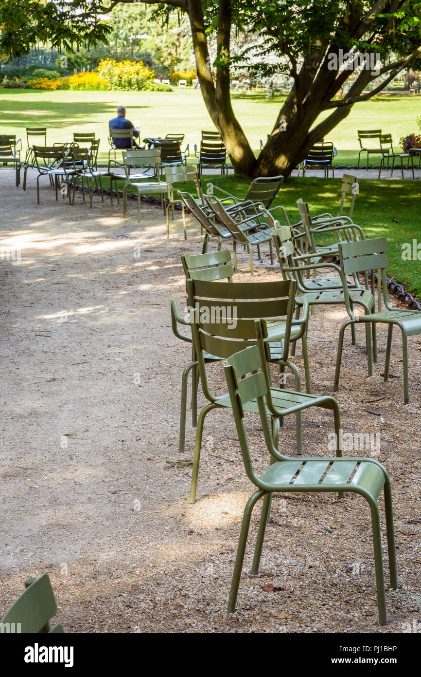 Ein Mann, der allein lesen, im Schatten sitzen auf einem Rasen Stuhl im Jardin du Luxembourg in Paris, Frankreich, mit sitzen entlang der Gassen zerstreut Stockfotografie