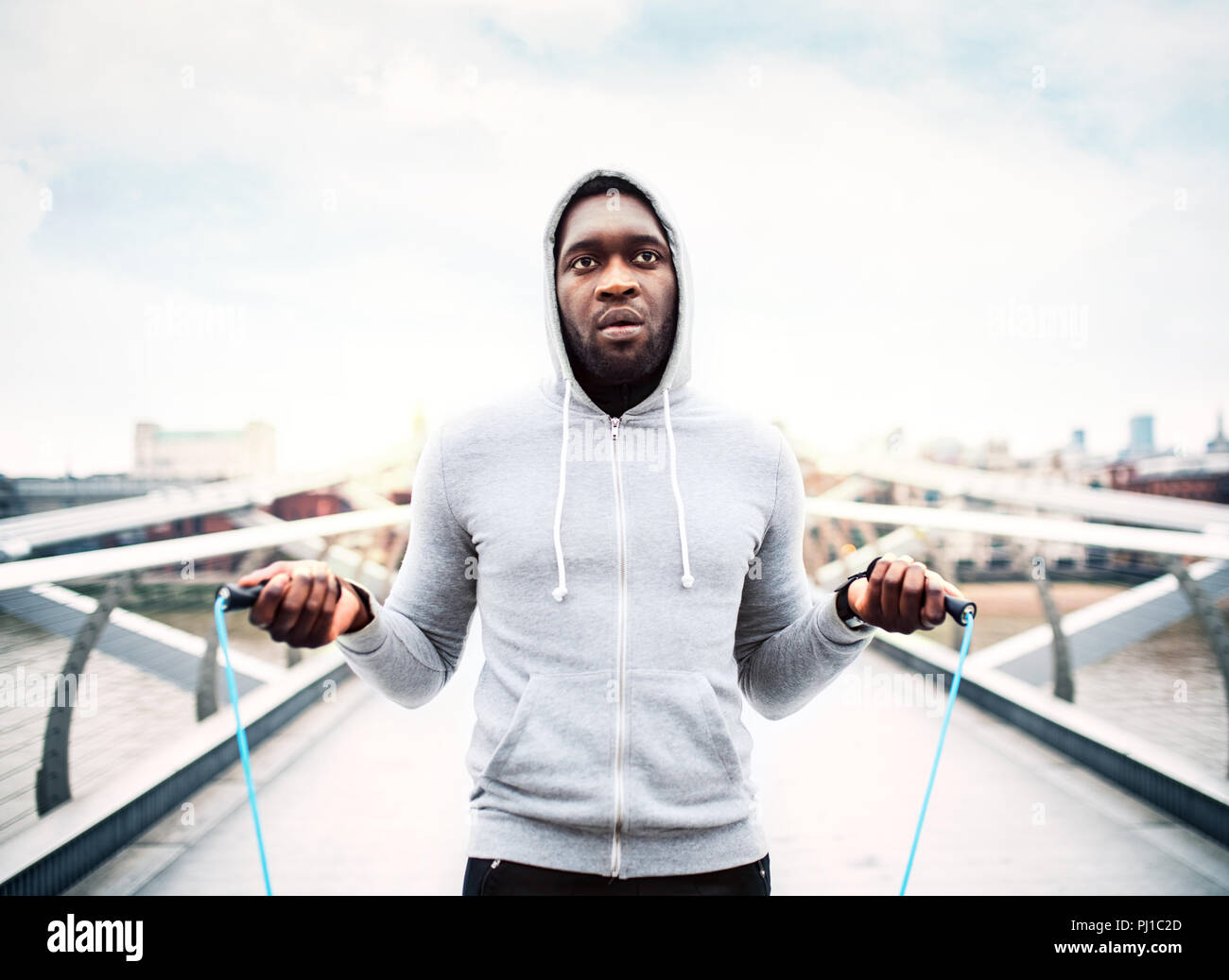 Junge aktive schwarze Sportler überspringt mit einem Seil in einer Stadt, hoodie tragen. Stockfoto