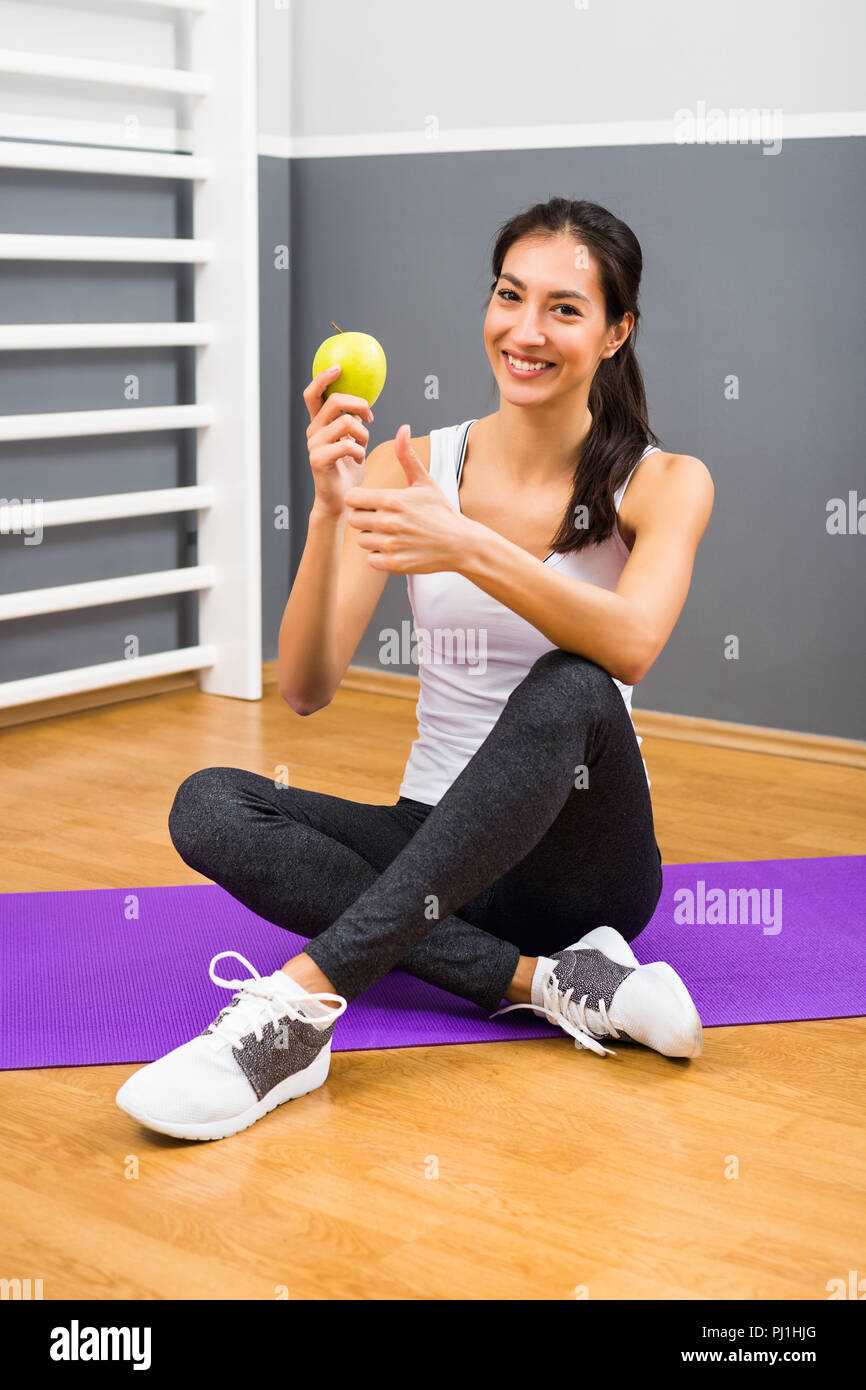 Schöne fitness Frau essen Apple und Daumen hoch an der Turnhalle Stockfoto
