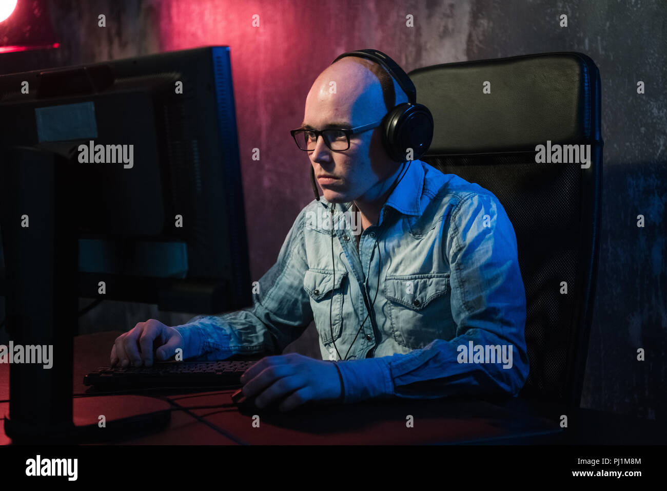 Ernster junger Mann sitzen und arbeiten mit Computer im dunklen Büro Stockfoto