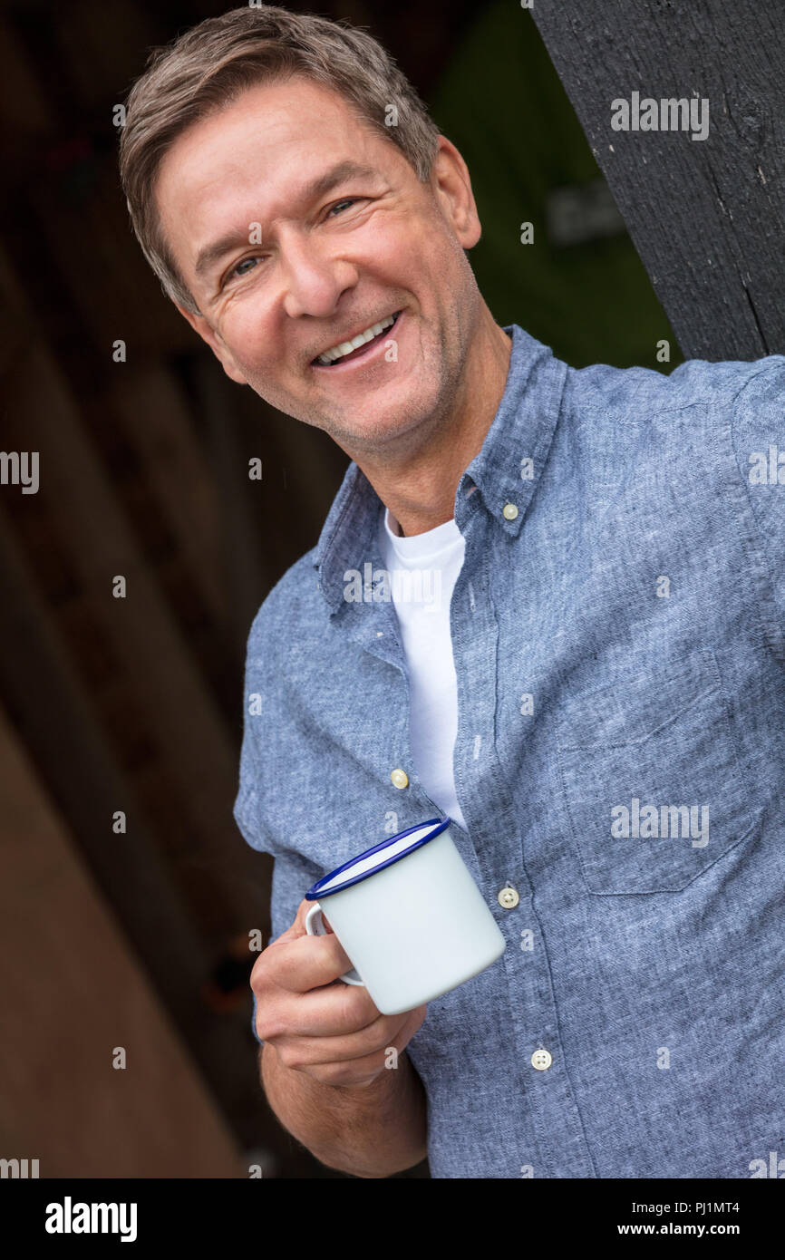 Porträt gedreht von einem attraktiven, erfolgreichen und glücklichen Mann mittleren Alters männlichen trägt ein blaues Hemd trinken Tee oder Kaffee aus einer Blechtasse Stockfoto