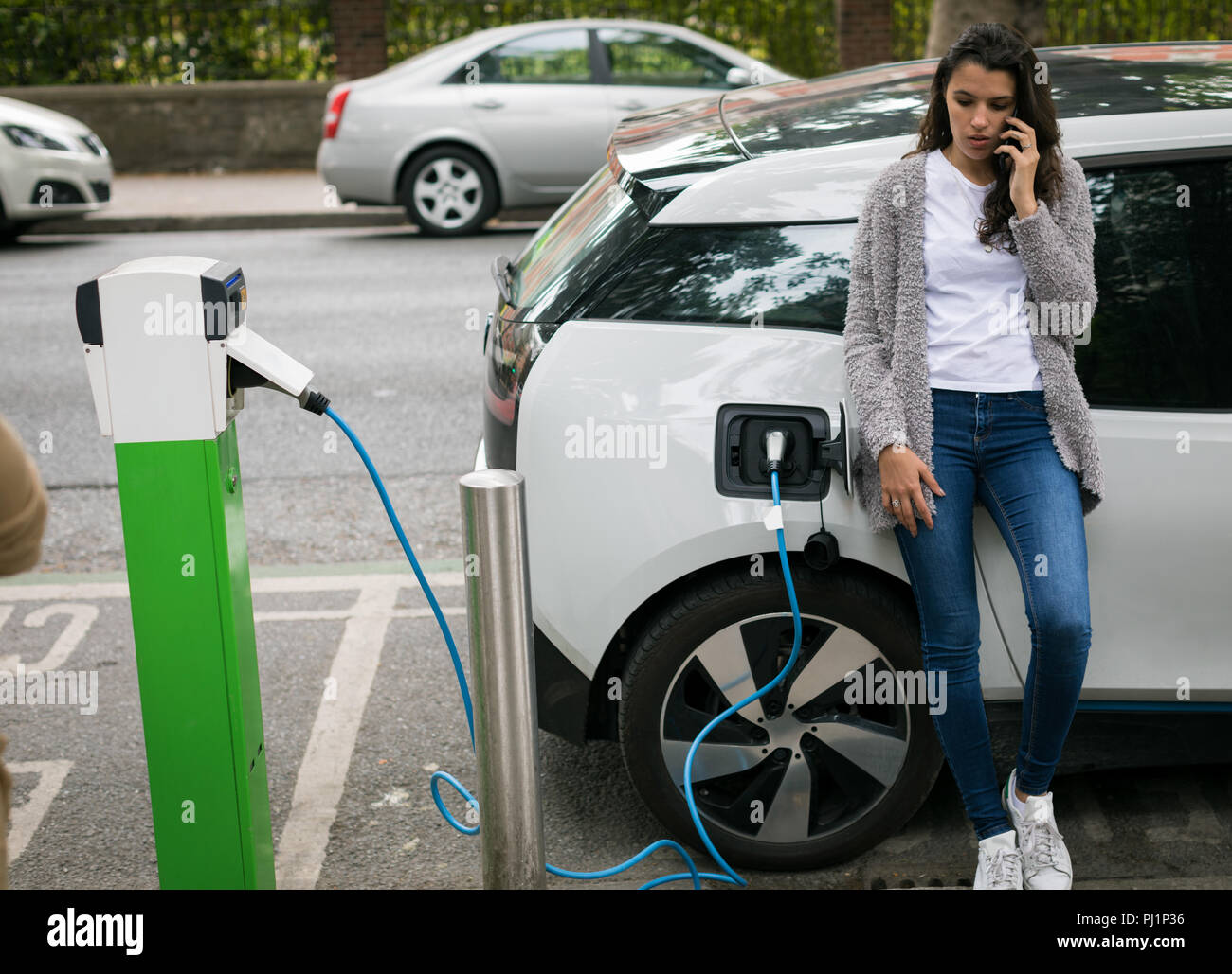 Frau Gespräch am Handy während des Ladevorgangs Elektroauto Stockfoto