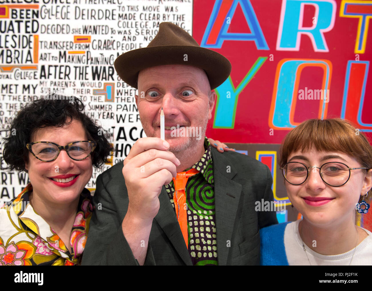 Royal Academy, London, UK. 4. September, 2018. Gefeierten Künstler Bob und Roberta Smith RA (Pseudonym erstellt von dem Künstler Patrick Brill) erscheint neben seiner neuen Anzeige an der Royal Academy. Das Geheimnis eines guten Lebens ist das erste Display, das durch einen Königlichen Akademiker im neu eröffneten Ronald und Rita McAulay Galerie, ein Ort, der für Standort-spezifischen Installationen durch Königlichen Akademiker. Foto: Der Künstler mit seiner Frau und seiner Tochter: Links, Künstlerin Jessica Voorsanger und, rechts, artist Etta Voorsanger-Brill. Credit: Malcolm Park/Alamy Leben Nachrichten. Stockfoto