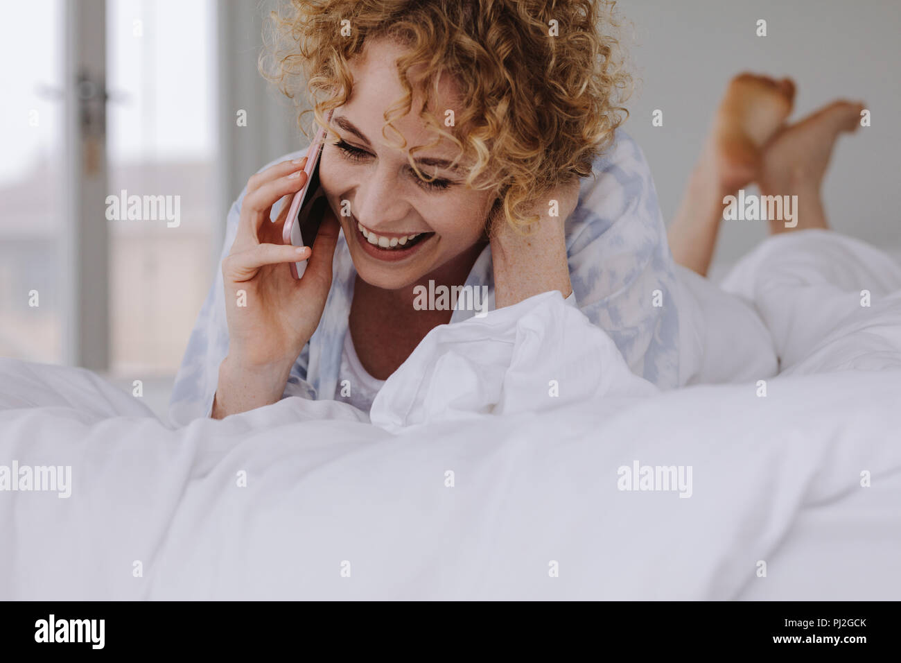 Frau Gespräch am Handy, während sie sich auf dem Bett. Frau Gespräch am Handy im Bett lag. Stockfoto