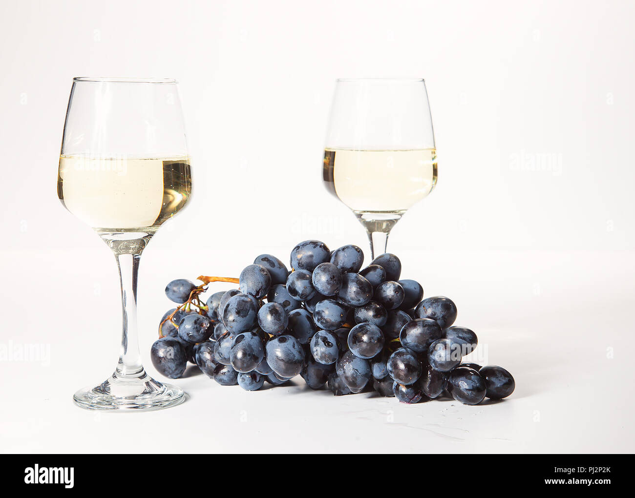 Zwei Gläser und eine Flasche Weißwein, auf einem weißen Hintergrund in der Nähe von einer Handvoll Trauben Stockfoto